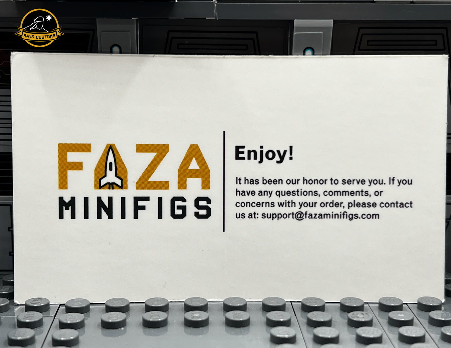 Faza Minifigs customer service card featuring the brand's logo with a rocket design and the message: 'Enjoy! It has been our honor to serve you. If you have any questions, comments, or concerns with your order, please contact us at support@fazaminifigs.com.' Displayed in a Star Wars-inspired diorama with a gray backdrop. Represents the brand's commitment to quality and customer satisfaction for custom LEGO minifigures