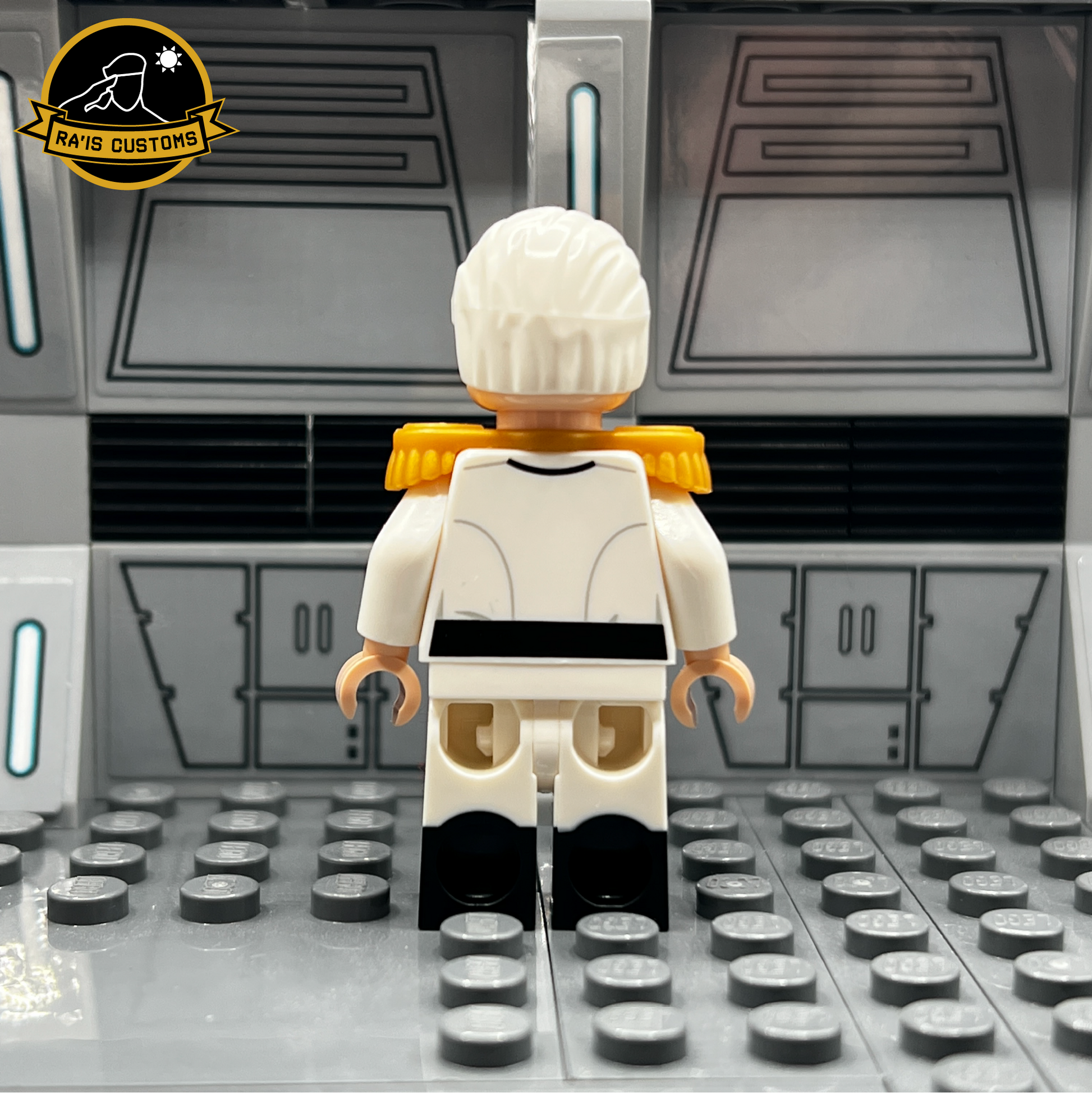 Rear view of the custom LEGO minifigure of Grand Admiral Pellaeon from Star Wars, created by Ra'is Customs. Showcases the back of the white uniform with gold epaulets and intricate detailing, highlighting the craftsmanship. Displayed in a Star Wars-inspired diorama with a futuristic gray backdrop, ideal for collectors and fans of high-quality custom LEGO figures.