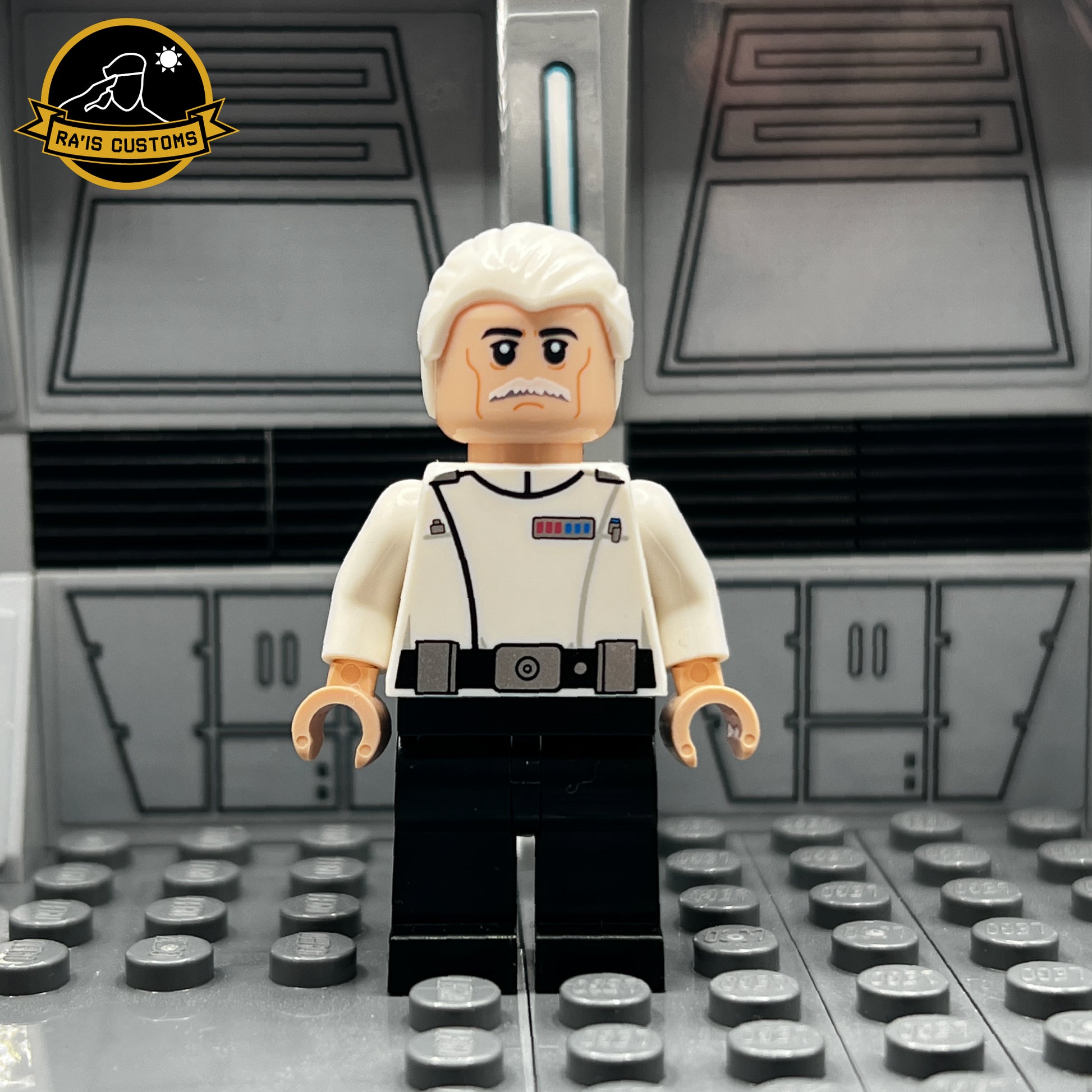 Pad-printed custom LEGO minifigure of Colonel Yularen from Star Wars, created by Ra'is Customs. Showcases a detailed Imperial uniform in white, complete with rank insignia, black belt, and a distinguished mustached facial design. Perfectly representing a key figure of the Galactic Empire, this figure is displayed in a Star Wars-themed diorama with a futuristic gray backdrop. Ideal for collectors and fans of high-quality custom LEGO minifigures seeking accurate Imperial designs.